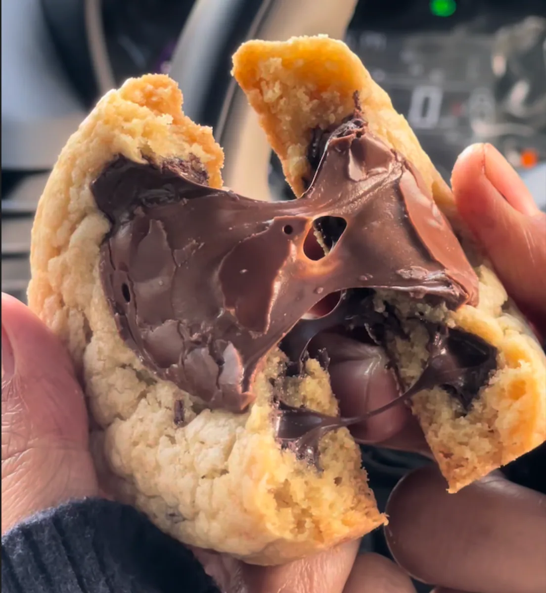 A chocolate chip cookie pulled in half, molten chocolate stretching between the pieces.