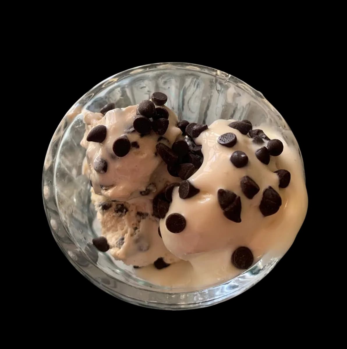 Cookie dough ice cream in a glass bowl, scattered with chocolate chips.