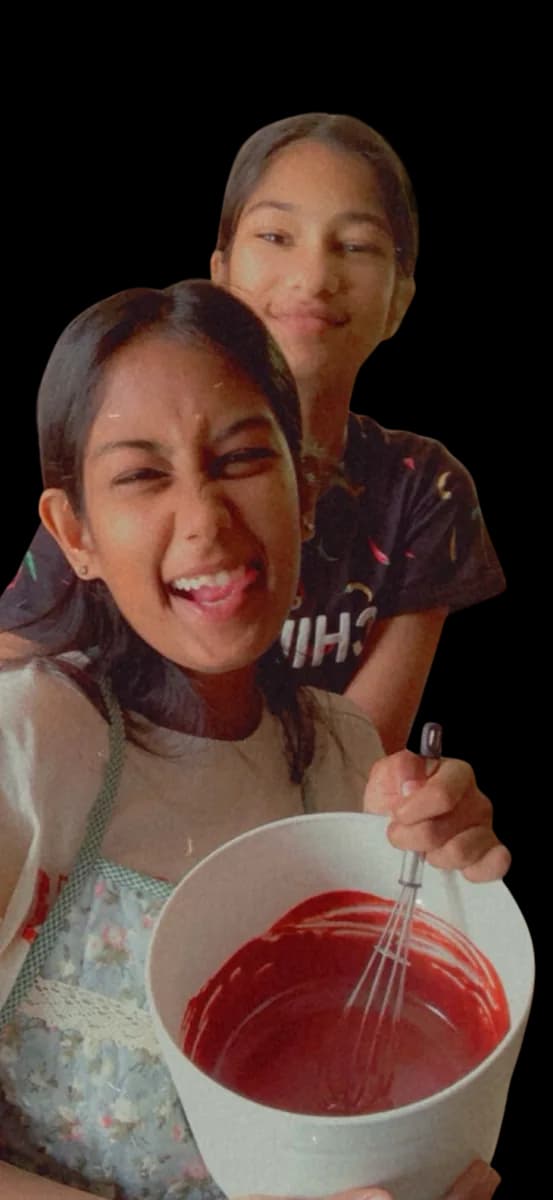 The two sisters laughing over a bowl of bright red cake batter.